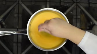 person stirring melted cheese on a stove